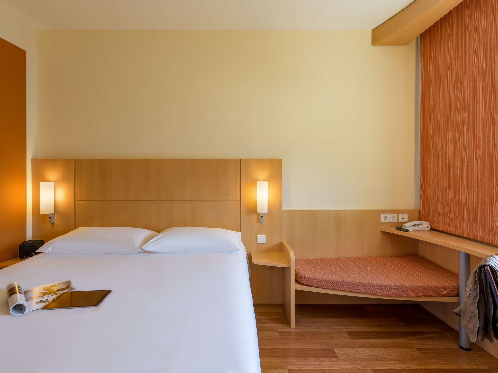Hotel room with two beds, wooden headboard, and warm wall lamps on a beige wall.